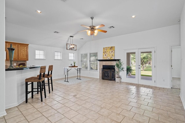 living area featuring a fireplace, ceiling fan with notable chandelier, baseboards, lofted ceiling, and visible vents