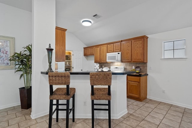 kitchen featuring visible vents, dark countertops, white microwave, a kitchen bar, and vaulted ceiling