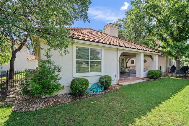 rear view of house with a lawn, ceiling fan, fence, and stucco siding