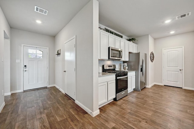 kitchen with visible vents, white cabinetry, dark wood finished floors, appliances with stainless steel finishes, and backsplash