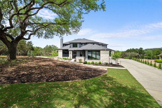 prairie-style house featuring a chimney, a front lawn, and stone siding