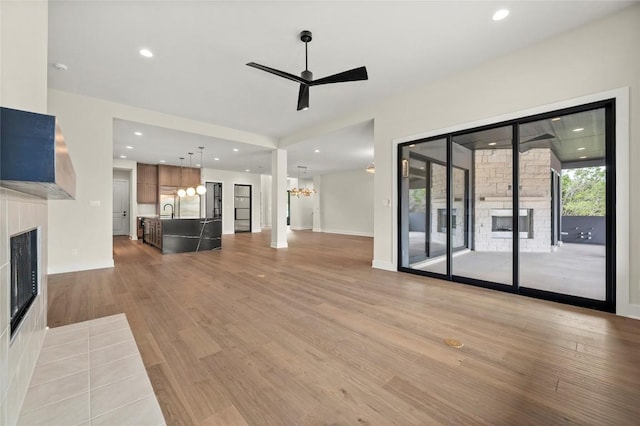 unfurnished living room featuring a fireplace, ceiling fan with notable chandelier, recessed lighting, and light wood-style flooring