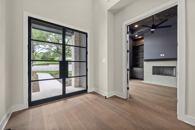 entryway with ceiling fan, a fireplace, built in shelves, wood finished floors, and baseboards