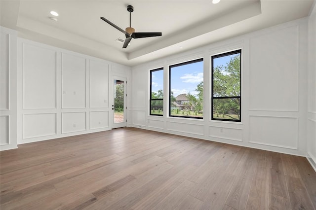 unfurnished bedroom featuring a raised ceiling, access to outside, a decorative wall, and light wood finished floors