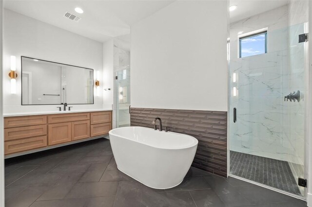 bathroom with a marble finish shower, vanity, tile walls, and visible vents