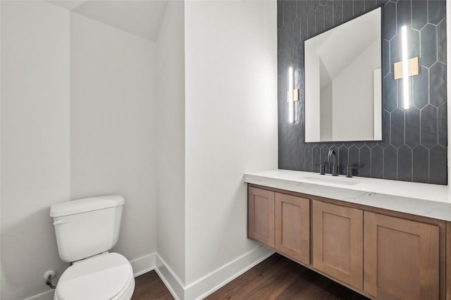 bathroom featuring decorative backsplash, wood finished floors, baseboards, vanity, and toilet