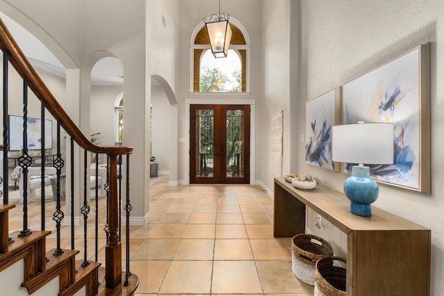 foyer entrance featuring baseboards, a high ceiling, stairway, arched walkways, and light tile patterned floors