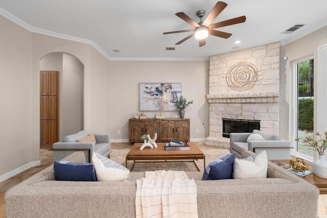 living room featuring visible vents, a ceiling fan, ornamental molding, a fireplace, and arched walkways