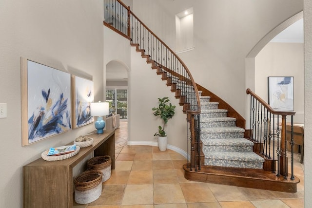 staircase featuring arched walkways, a high ceiling, baseboards, and tile patterned floors