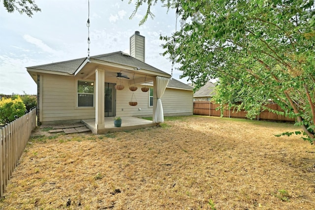 back of property featuring a fenced backyard, a chimney, a patio area, a lawn, and a ceiling fan