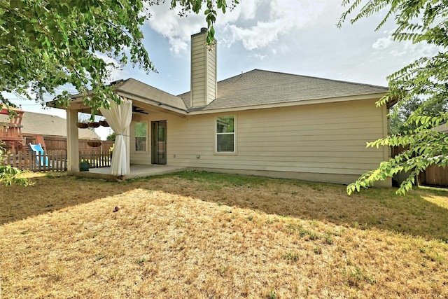 rear view of house featuring fence, a chimney, a lawn, and a patio area