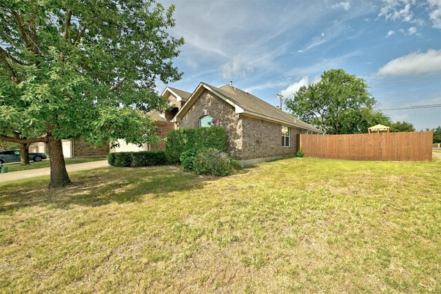 view of side of property featuring brick siding, a lawn, and fence