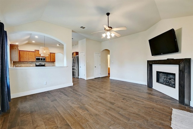 unfurnished living room featuring ceiling fan, visible vents, arched walkways, a glass covered fireplace, and vaulted ceiling