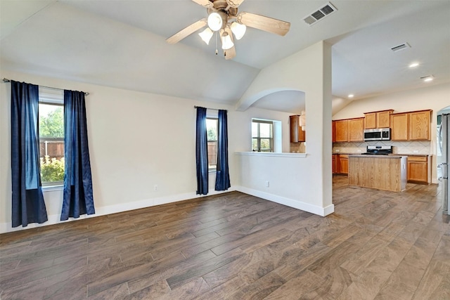 unfurnished living room with ceiling fan, visible vents, arched walkways, wood finished floors, and vaulted ceiling
