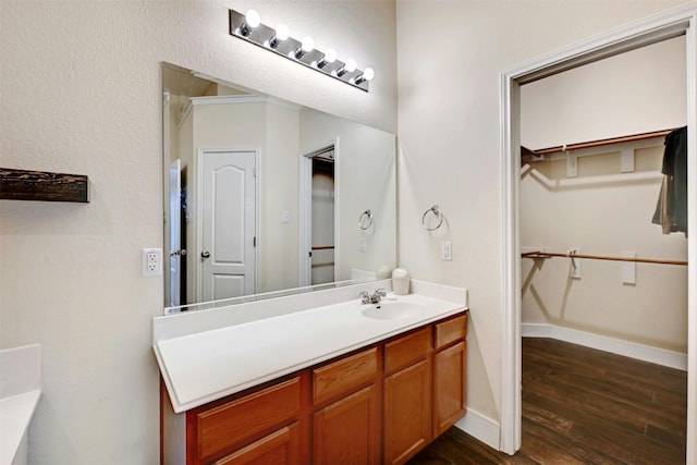 full bath with vanity, baseboards, a walk in closet, and wood finished floors