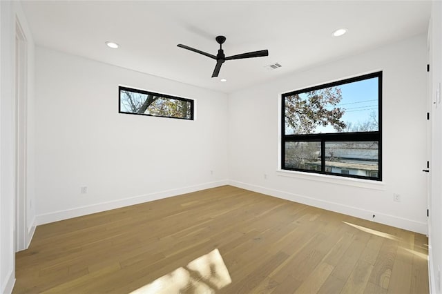 empty room featuring visible vents, ceiling fan, wood finished floors, and a wealth of natural light
