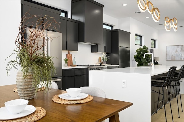 kitchen featuring a sink, light countertops, dark cabinets, a kitchen bar, and pendant lighting
