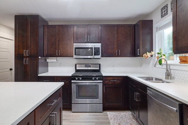 kitchen with appliances with stainless steel finishes, a sink, light wood finished floors, light countertops, and decorative backsplash