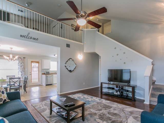 living room with high vaulted ceiling, wood finished floors, stairway, and ceiling fan with notable chandelier