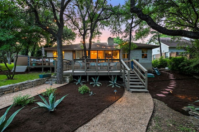back of house at dusk featuring brick siding, a chimney, stairs, and a deck