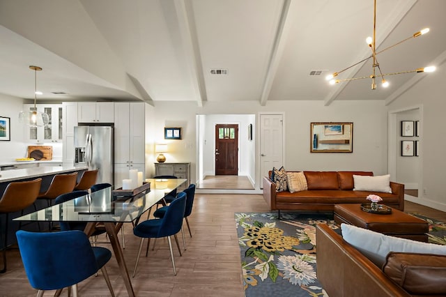 living area featuring visible vents, light wood-style flooring, vaulted ceiling with beams, and an inviting chandelier