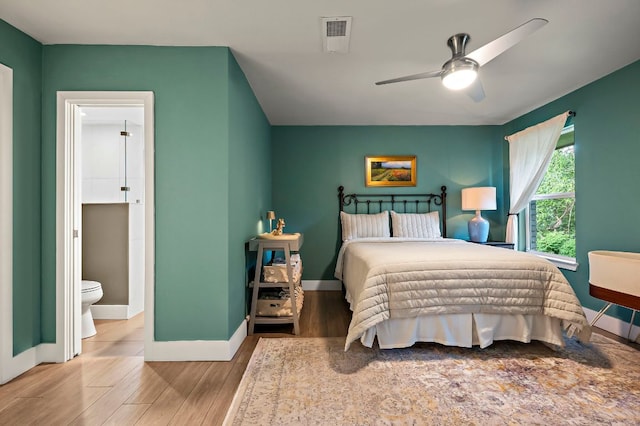 bedroom featuring baseboards, ceiling fan, wood finished floors, and ensuite bath