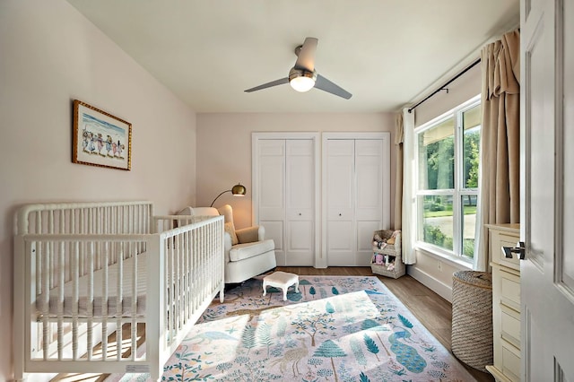 bedroom featuring multiple closets, wood finished floors, baseboards, ceiling fan, and a nursery area