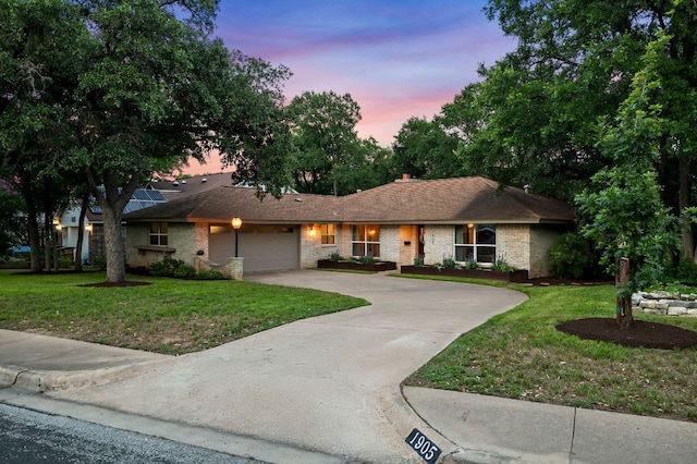 single story home featuring a yard, brick siding, driveway, and a garage