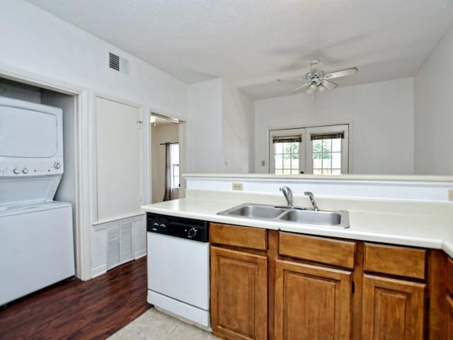 kitchen with brown cabinetry, white dishwasher, a sink, and stacked washer / dryer