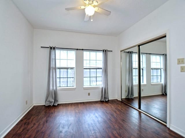 unfurnished bedroom featuring baseboards, multiple windows, wood finished floors, and a closet