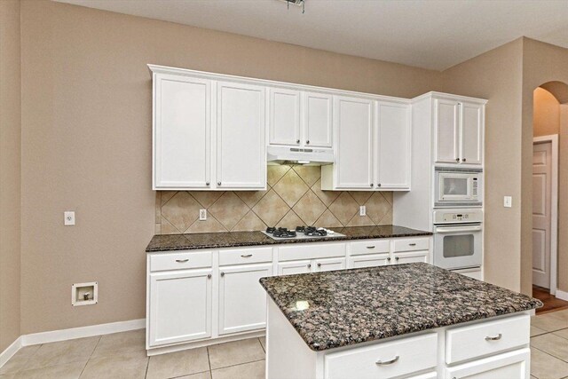3705 Derby Trl, Round Rock, TX 78681 - kitchen with white appliances, under cabinet range hood, arched walkways, dark stone counters, and tasteful backsplash