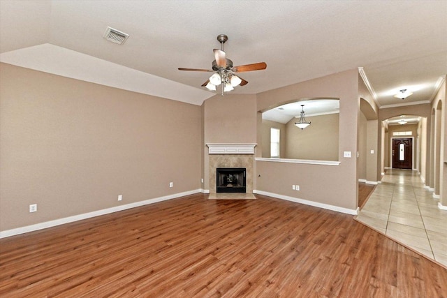 3705 Derby Trl, Round Rock, TX 78681 - unfurnished living room featuring arched walkways, light wood-type flooring, ceiling fan, a tiled fireplace, and ornamental molding