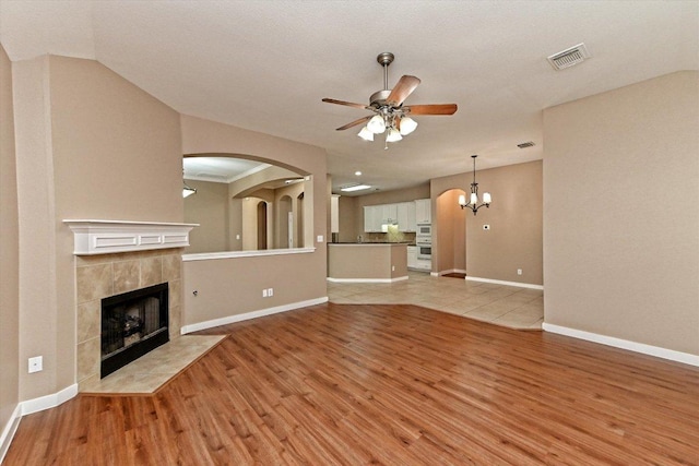 3705 Derby Trl, Round Rock, TX 78681 - unfurnished living room with ceiling fan, light wood finished floors, a tiled fireplace, arched walkways, and lofted ceiling