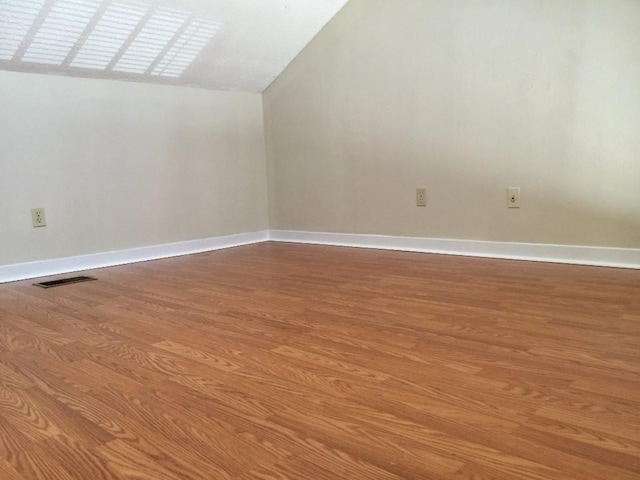 interior space featuring visible vents, baseboards, wood finished floors, and vaulted ceiling