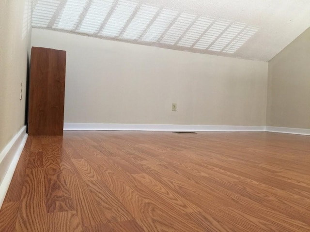 spare room featuring baseboards, lofted ceiling, and wood finished floors