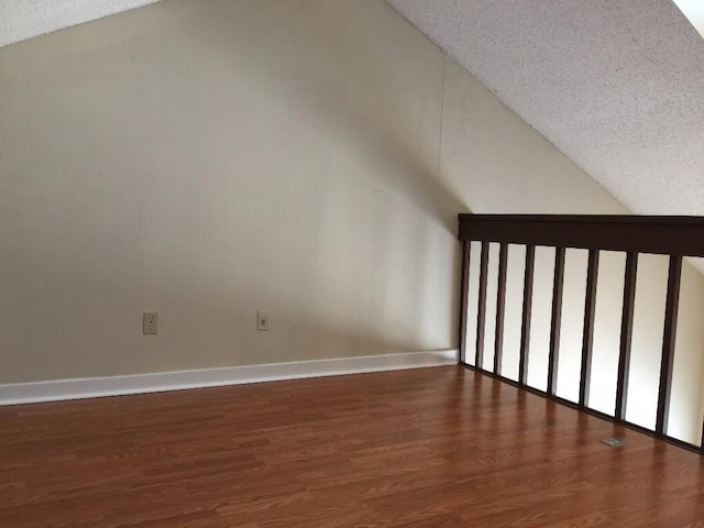 bonus room featuring wood finished floors, baseboards, a textured ceiling, and lofted ceiling