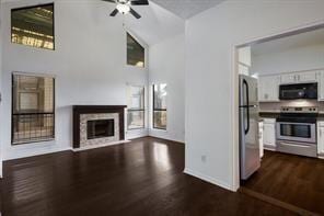 unfurnished living room featuring ceiling fan, dark wood-style flooring, a fireplace, vaulted ceiling, and baseboards