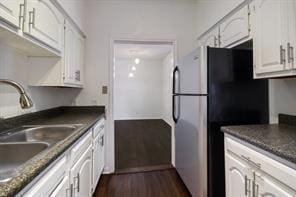 kitchen with freestanding refrigerator, dark countertops, dark wood-style floors, white cabinets, and a sink