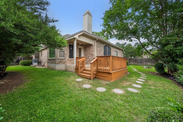 rear view of house with a chimney, brick siding, central AC, fence, and a yard