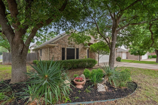view of property hidden behind natural elements with an attached garage, fence, driveway, and brick siding