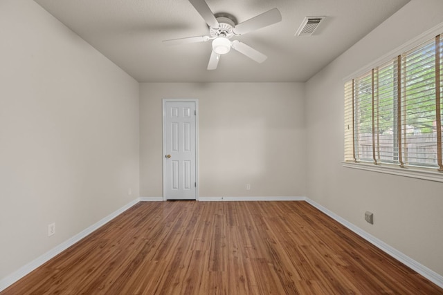 empty room with baseboards, a ceiling fan, wood finished floors, and visible vents