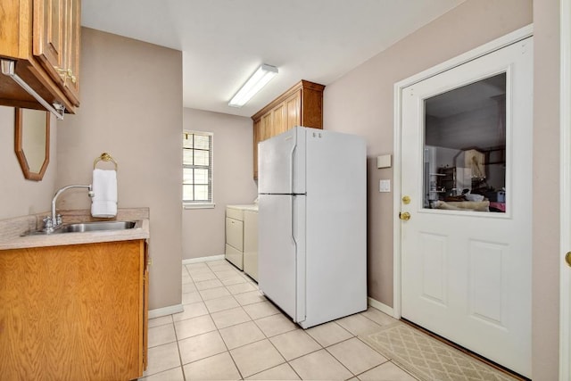 kitchen featuring freestanding refrigerator, baseboards, light countertops, a sink, and light tile patterned floors