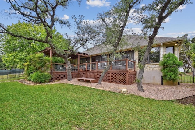 rear view of house with a lawn, fence, a wooden deck, and roof with shingles
