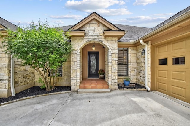 doorway to property featuring an attached garage, roof with shingles, and stone siding