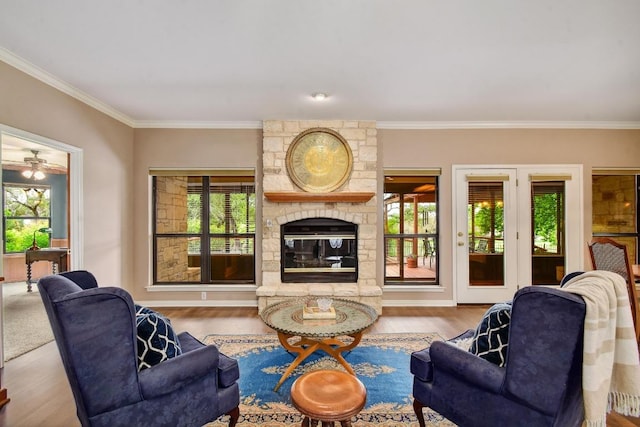 living room with crown molding, a stone fireplace, a wealth of natural light, and wood finished floors