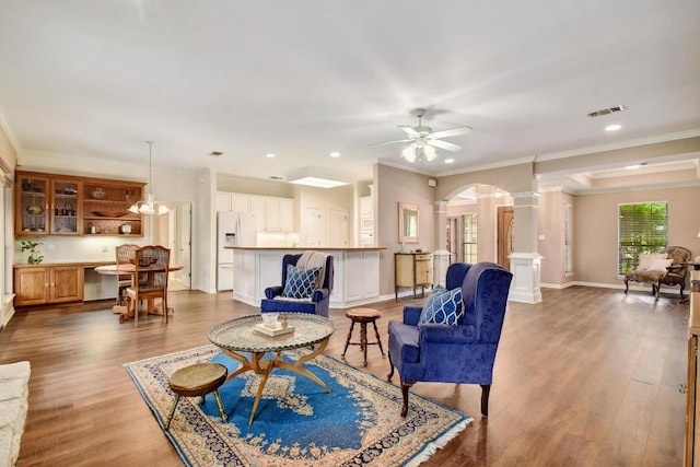 living area featuring a ceiling fan, crown molding, arched walkways, wood finished floors, and ornate columns