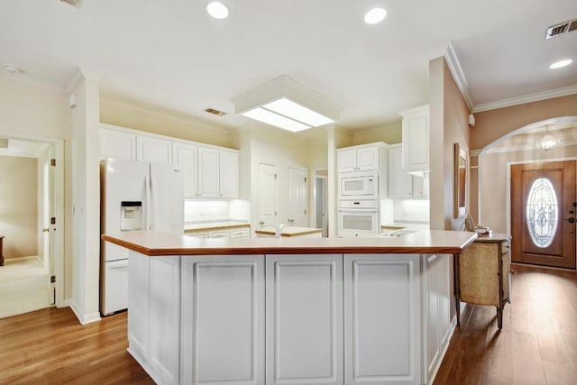 kitchen featuring a large island, visible vents, arched walkways, white cabinets, and white appliances