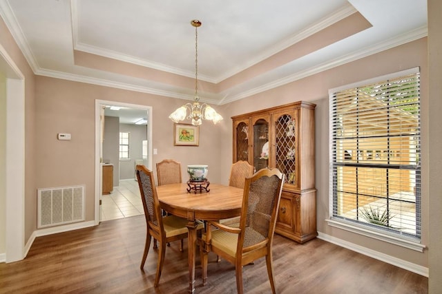 dining room featuring visible vents, wood finished floors, a raised ceiling, baseboards, and a chandelier