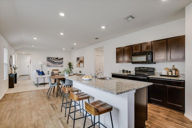 15005 Bajada Rd, Manor, TX 78653 - kitchen with black appliances, a sink, a breakfast bar area, recessed lighting, and a center island with sink