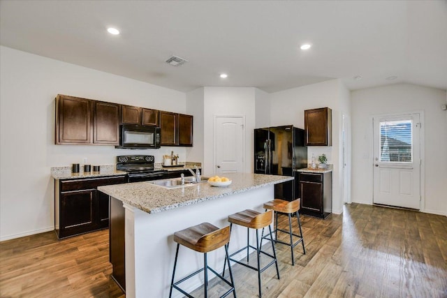 15005 Bajada Rd, Manor, TX 78653 - kitchen featuring black appliances, a sink, a kitchen bar, dark brown cabinets, and wood finished floors